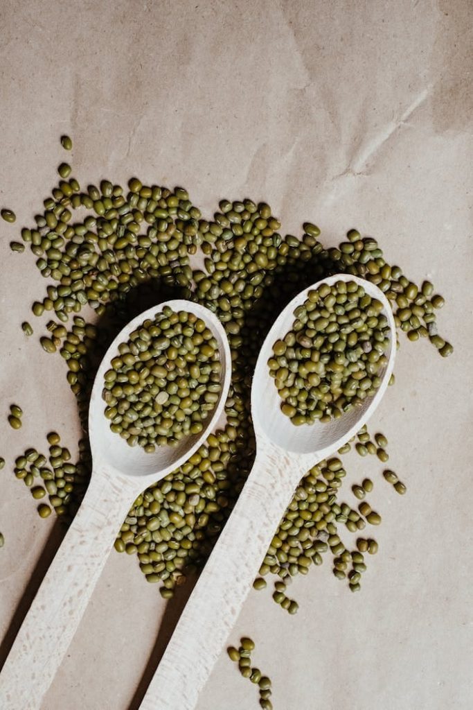 Top view of organic mung beans in wooden spoons on brown paper background.